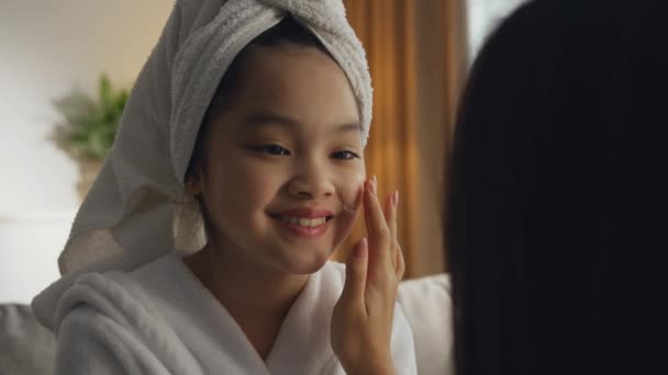 Zoom en el retrato de la madre aplicando crema hidratante en su cara hija asiática, enseñando a la niña a preocuparse por la piel — Vídeo de stock