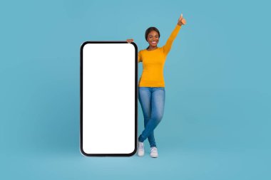 Heyecanlı siyahi kadın Büyük Boş Akıllı Telefonun yanında duruyor ve Başparmağını kaldırıyor