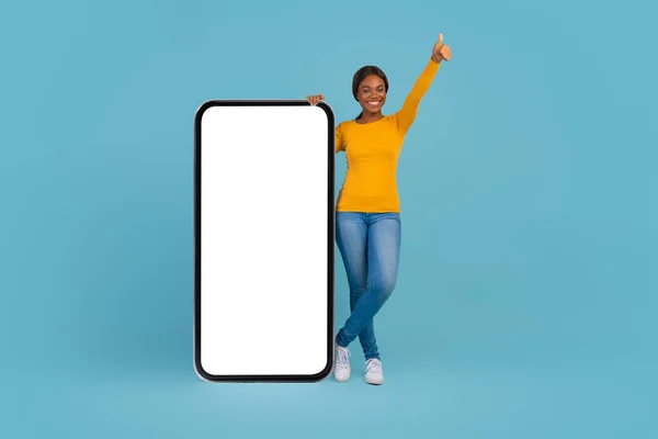 兴奋的黑人女士站在大块空白智能手机附近，把拇指伸出来 — 图库照片