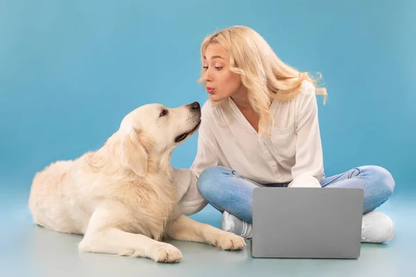 Ung kvinna med dator sittandes på golvet kysser glad hund — Stockfoto