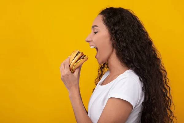 Senhora engraçada segurando hambúrguer mordendo sanduíche no estúdio — Fotografia de Stock