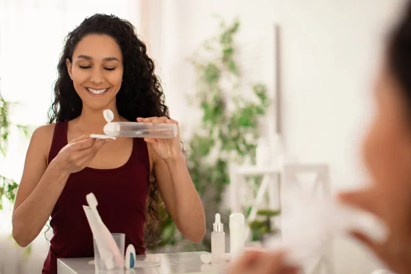 Bella giovane donna che rimuove il trucco con lozione o tonico, utilizzando pad di cotone davanti allo specchio in bagno, spazio vuoto — Foto Stock