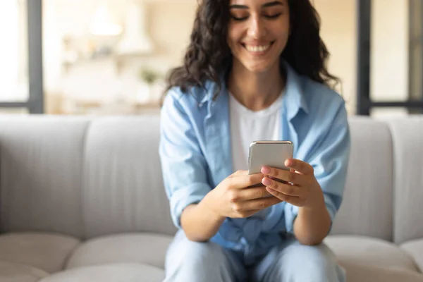 스마트폰을 사용하는 긍정적 인 젊은 여성, 집에서 소파에 앉아 선택적 인 집중을 하는 여성 — 스톡 사진
