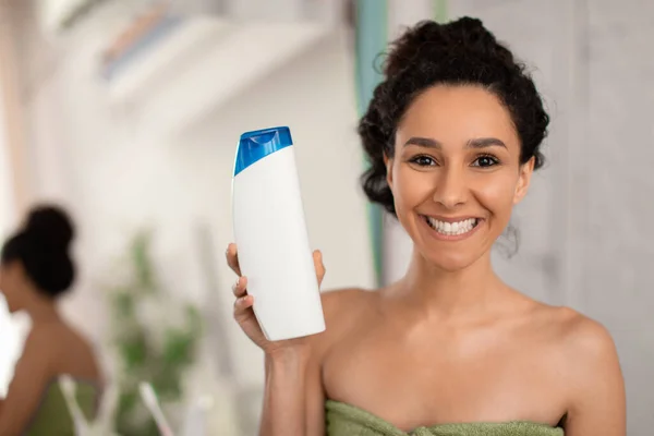 Lächelnde Frau zeigt Shampoo-Flasche mit Design-Attrappe vor der Kamera, wirbt für Haarpflegelotion oder Duschgel — Stockfoto