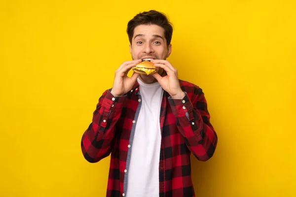 Divertido tipo hambriento sosteniendo hamburguesa mordiendo sándwich en el estudio — Foto de Stock