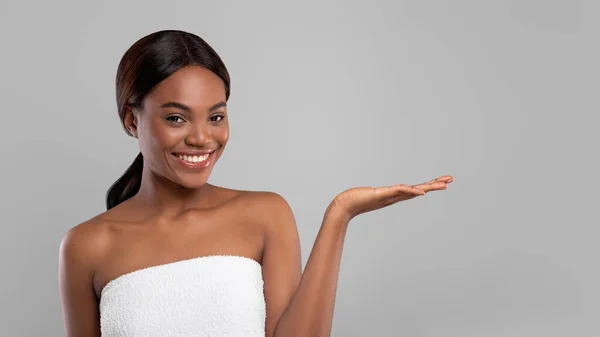 Pubblicità di bellezza. felice nero donna in asciugamano tenendo qualcosa su vuoto palmo — Foto Stock