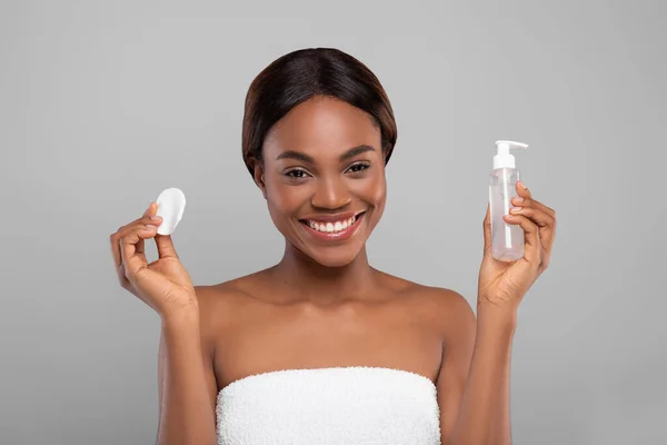 Pamuk pedi ve yüz temizleme jeliyle şişeyi tutan mutlu siyah kadın. — Stok fotoğraf