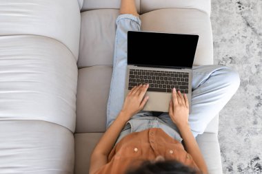 Genç bayanın evdeki kanepesinde boş ekranı olan dizüstü bilgisayarı kullanışının en üst görüntüsü, web sitesi veya reklam için modelleme