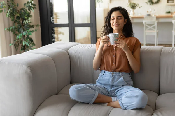 Tranquillo giovane donna bruna seduta sul divano con gli occhi chiusi, bere caffè caldo a casa, copiare spazio — Foto Stock