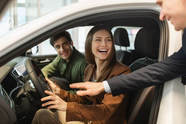 幸せな若いカップルのテストは新しい車を運転し、セールスマンは彼らが自動車販売店で最良の選択をするのを助ける — ストック写真