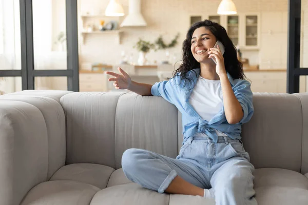 Glad tusenårig brunett kvinna sitter på soffan, ringa på mobiltelefon hemma, ledigt utrymme — Stockfoto