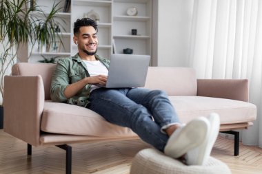 Evde dizüstü bilgisayarda çalışan ve kulaklıkla müzik dinleyen Arap bir serbest yazar.