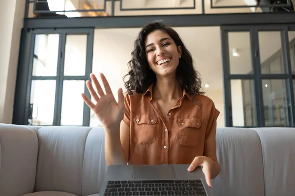 Mulher nova encantadora com laptop se comunicando on-line, acenando na webcam, sentado no sofá em casa, espaço de cópia — Fotografia de Stock