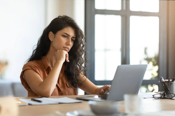 Tänksam ung brunett kvinna tittar på bärbar skärm, arbetar online vid skrivbordet i hemmakontoret, gratis utrymme — Stockfoto