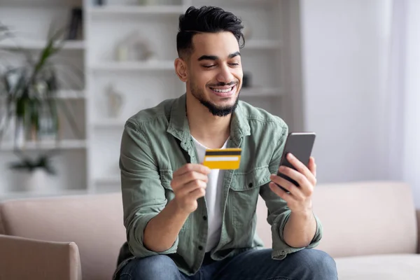 Happy Przystojny Bliski Wschód Guy zakupy online ze smartfonem i kartą kredytową — Zdjęcie stockowe