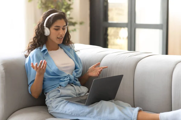 Ganska tusenårig kvinna i hörlurar kommunicerar online på bärbar dator, med videokonferens inomhus, gratis utrymme — Stockfoto