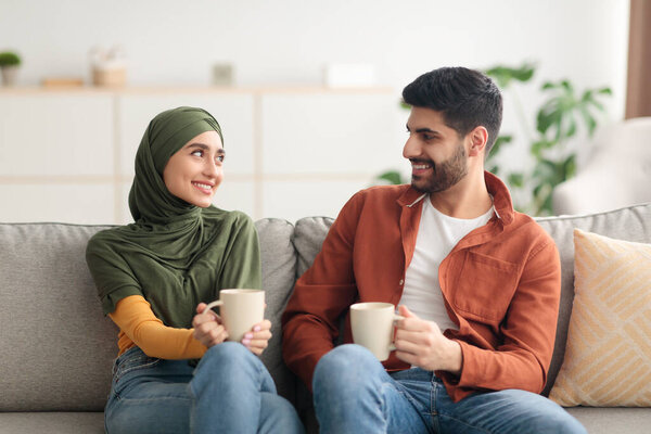 Happy Arabic Spouses Holding Mugs Drinking Coffee Sitting At Home