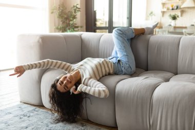 Kulaklıklı güzel bir kadın kanepeye uzanıp müzik dinliyor, evde dinleniyor.