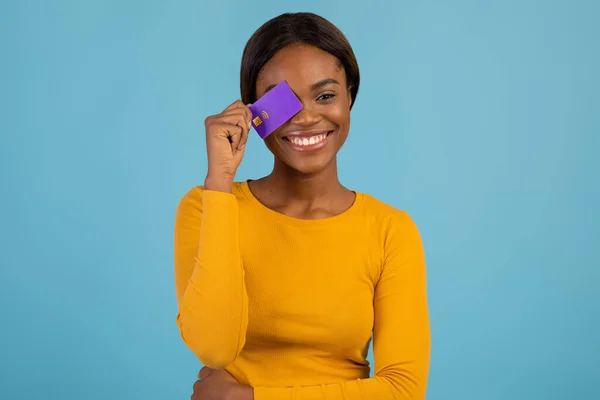 Pagamentos fáceis. Jovem mulher afro-americana alegre que cobre o olho com cartão de crédito — Fotografia de Stock