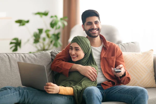 Cônjuges do Oriente Médio usando laptop e assistindo televisão em casa — Fotografia de Stock