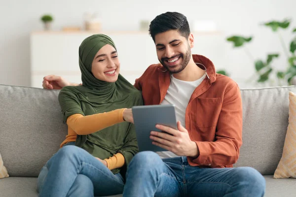 Cônjuges felizes do Oriente Médio usando tablet digital sentado em casa — Fotografia de Stock