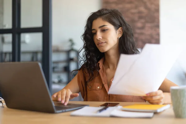 Konzentrierte junge Geschäftsfrau, die am Laptop arbeitet oder studiert, Dokumente hält, drinnen am Schreibtisch sitzt, Kopierraum hat — Stockfoto