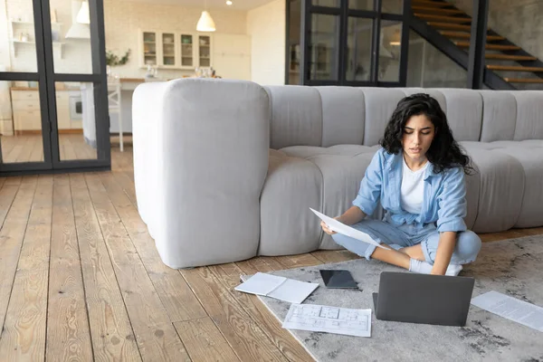 Fokuserad ung kvinna som arbetar på nätet, studerar finansiella dokument, använder bärbar dator hemma, ledigt utrymme — Stockfoto