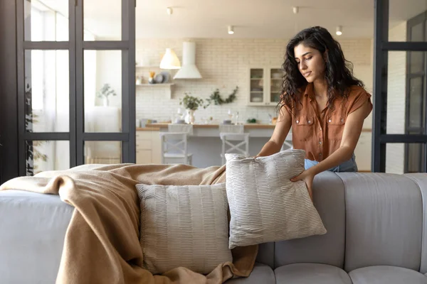 Attraktiv ung kvinna ordna kuddar och rutig på bekväm soffa, vilket gör hennes hem mysig, tomt utrymme — Stockfoto