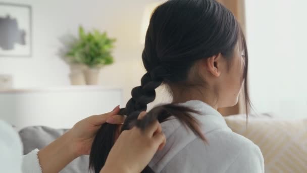 Salon kecantikan domestik. Ibu tak dikenal yang peduli membuat gaya rambut kepang untuk putri kecilnya di rumah. — Stok Video