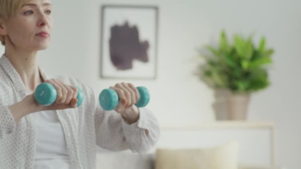 Réadaptation et entraînement physique. Gros plan portrait d'une femme faible d'âge moyen faisant de l'exercice avec de petits haltères — Video