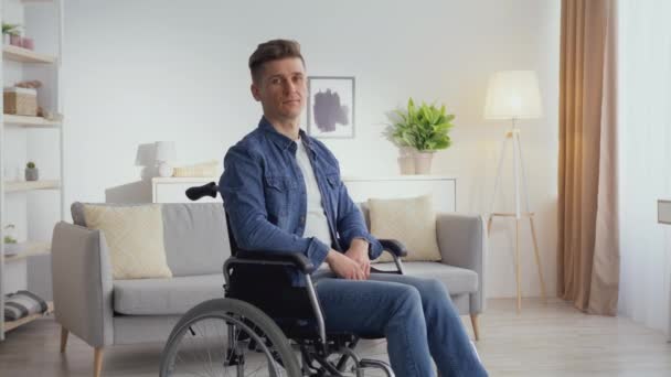 Спокойный зрелый мужчина с травмой позвоночника сидит в инвалидной коляске и смотрит в камеру, позирует в интерьере дома, отслеживает выстрел — стоковое видео