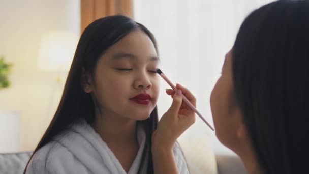 Любящая мать делает профессиональный макияж для своей маленькой азиатской дочери, играя салон красоты дома, замедленной съемки — стоковое видео