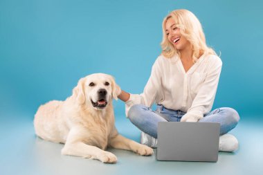 Genç bir kadın yerde oturmuş mutlu köpeği okşuyor.