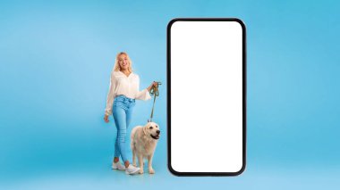 Büyük akıllı telefonun yanında köpeğini gezdiren genç bir kadın.