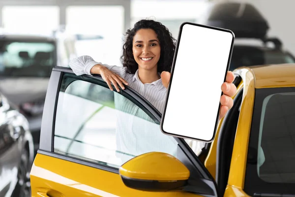 Pozytywna kobieta z Bliskiego Wschodu stojąca samochodem, pokazująca smartfon — Zdjęcie stockowe