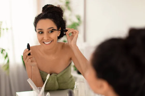 Concepto de rutina de belleza matinal. Atractiva joven aplicación de rímel, mirando en el espejo en casa, espacio de copia — Foto de Stock