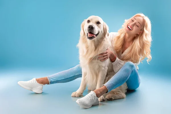 Jovem mulher coçando seu cão no estúdio azul — Fotografia de Stock