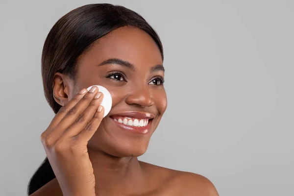 Sorrindo atraente preto senhora limpeza rosto com almofada de algodão, tiro de close-up — Fotografia de Stock