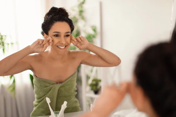Wanita muda yang cantik membuat drainase limfatik pijat wajah di dekat cermin di rumah, ruang kosong — Stok Foto
