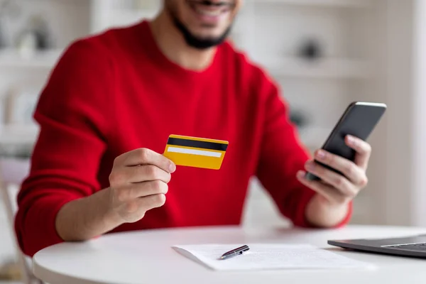 Płacenie rachunków online. Arab korzystający ze smartfona i karty kredytowej w domu — Zdjęcie stockowe