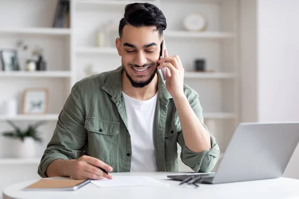 Handsome Arab Male Freelancer Talking On Handy And Taking Notes At Home — Stockfoto