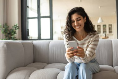 Milenyum Kafkasyalı kadın koltukta otururken akıllı telefon kullanıyor, mesajları kontrol ediyor, evde video görüşmesi yapıyor.