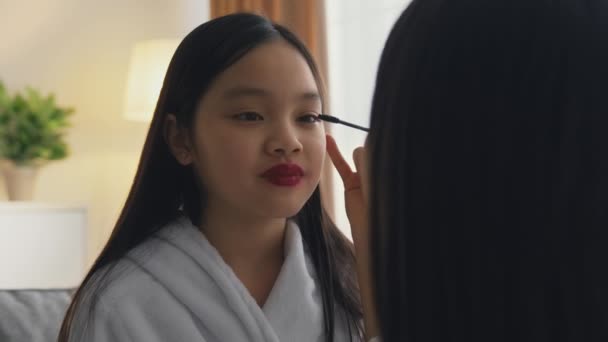 Sentirse adulto. Madre cariñosa haciendo ceremonial maquillaje a su pequeña hija asiática, feliz chica bonita sonriendo — Vídeo de stock