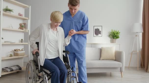 专业的男性治疗师帮助成熟的女性从轮椅上站起来行走，在事故后变得健康 — 图库视频影像