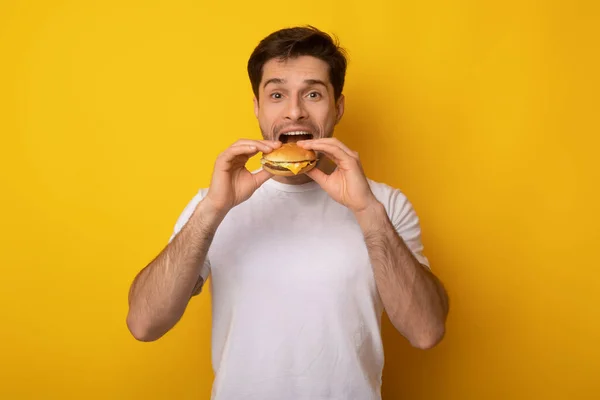 Divertido chico sosteniendo hamburguesa mordiendo sándwich en el estudio — Foto de Stock