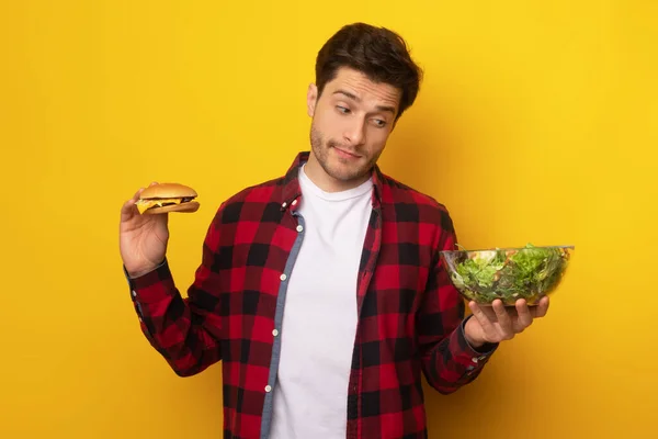 Retrato de cara engraçado segurando hambúrguer e salada de legumes — Fotografia de Stock