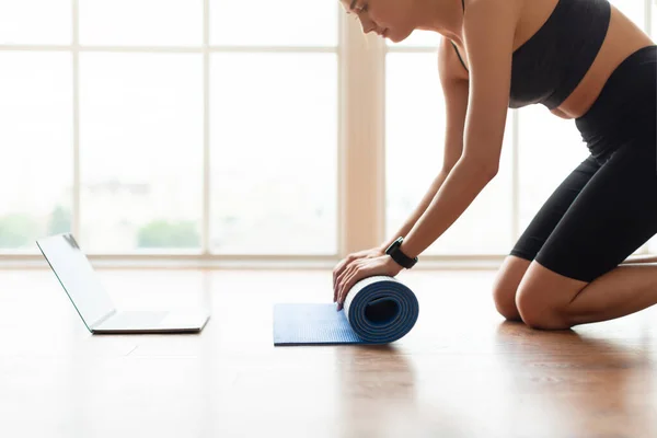 Молодая женщина разворачивает коврик для йоги на полу возле ноутбука — стоковое фото