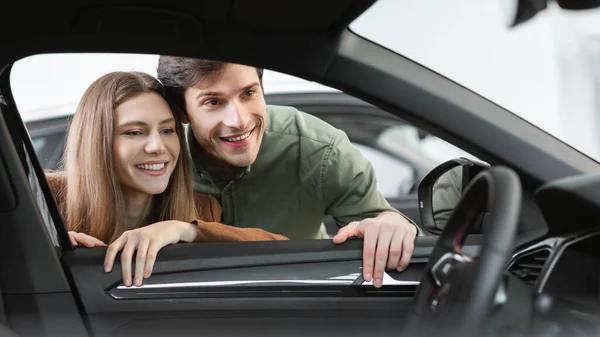 Vidám fiatal férfi és nő vásárol új autót, ellenőrzi autószalon az ablakon keresztül, panoráma — Stock Fotó