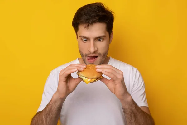 Lustiger junger Kerl mit Blick auf Burger im Studio — Stockfoto