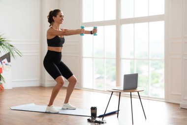 Genç bir kadın emniyet müdürünün önünde dambıllarla egzersiz yapıyor.